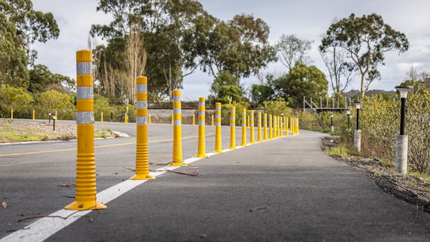 A winding road flanked by yellow safety posts with trees in the backdrop, perfect for roadway themes.